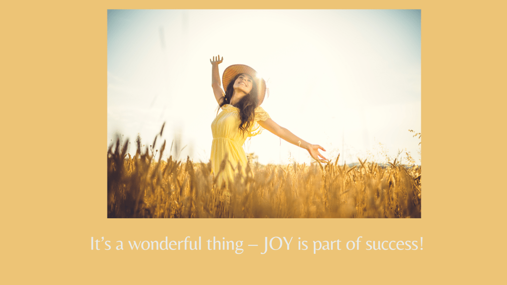Picture of a brightly smiling woman wearing a yellow sleeveless dress and straw hat. She's standing in a field of wheat on a sunny day with her hands and head thrown back. 